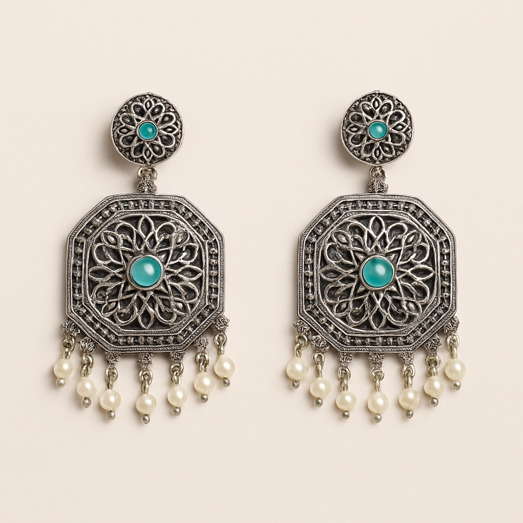 Ornate silver earrings with turquoise stones and pearl-like beads on a beige background