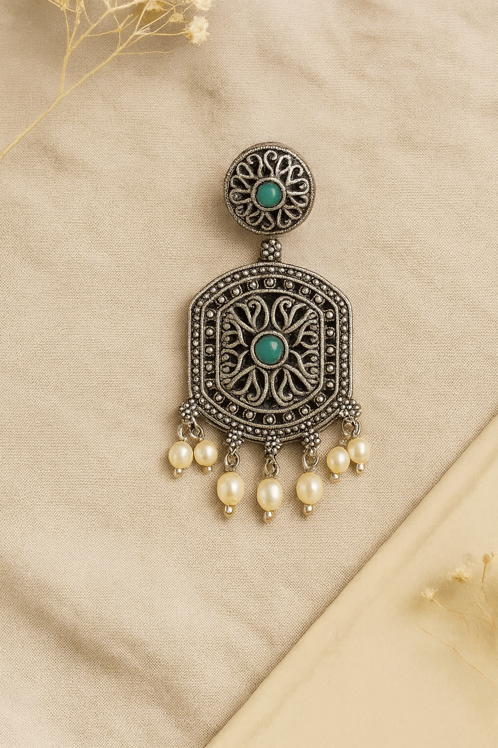 Ornate earring with pearls and green gemstones on a beige fabric background